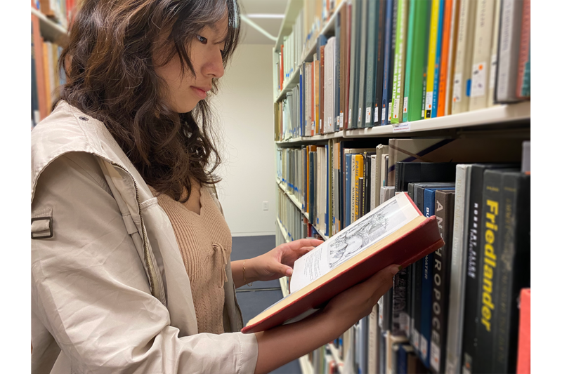 A person standing in library stacks looking at a book.